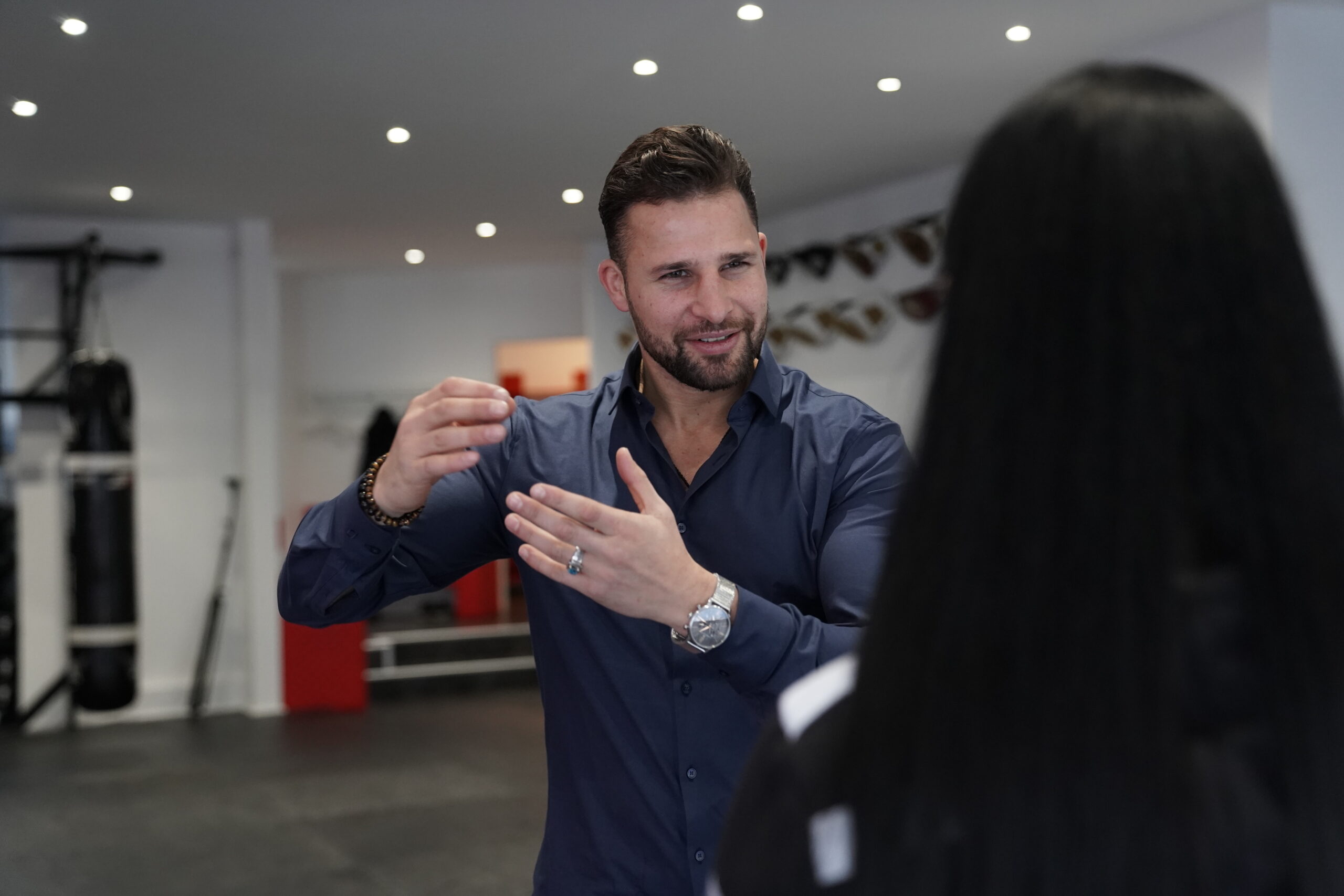 Max Baumert erklärt einer Klientin im Gym etwas im Coaching-Gespräch